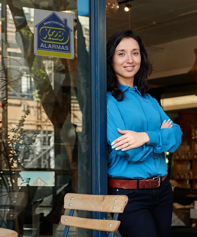 Joven sonriente al frente de su negocio, feliz y segura por contar con la protección monitoreada en su comercio
